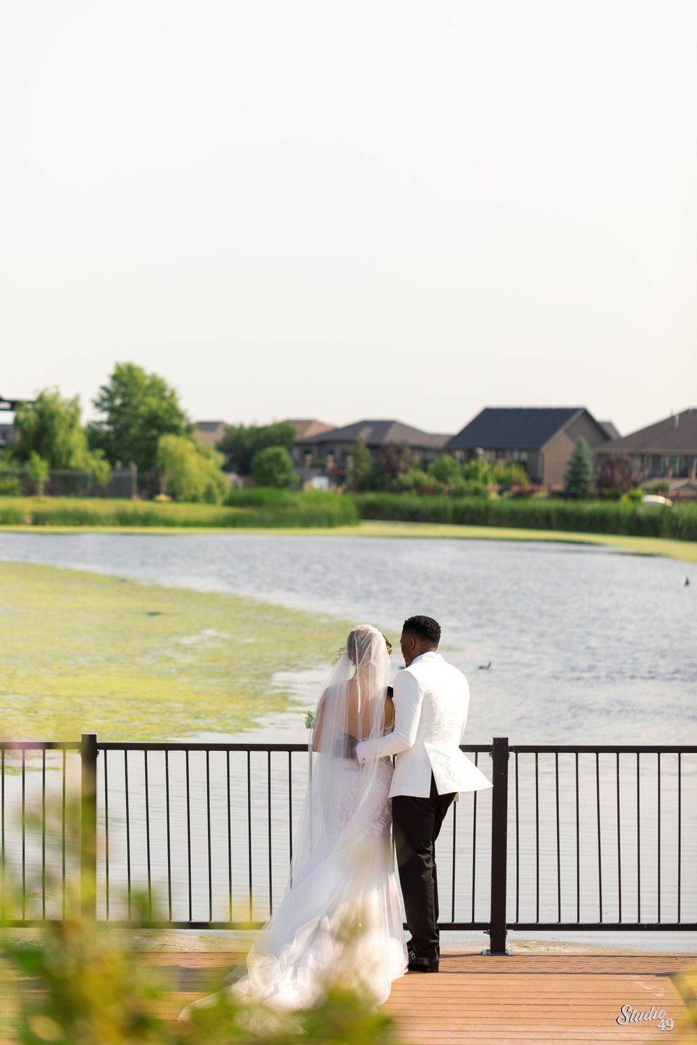 Bride and groom standing together on waterfront deck overlooking scenic lake.