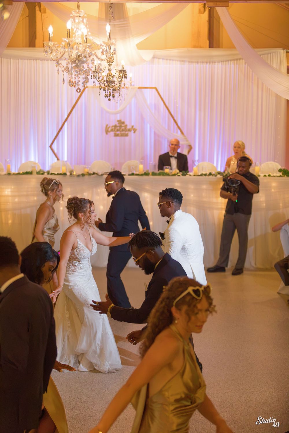 Bride and groom dancing joyfully with guests at elegant white wedding reception.