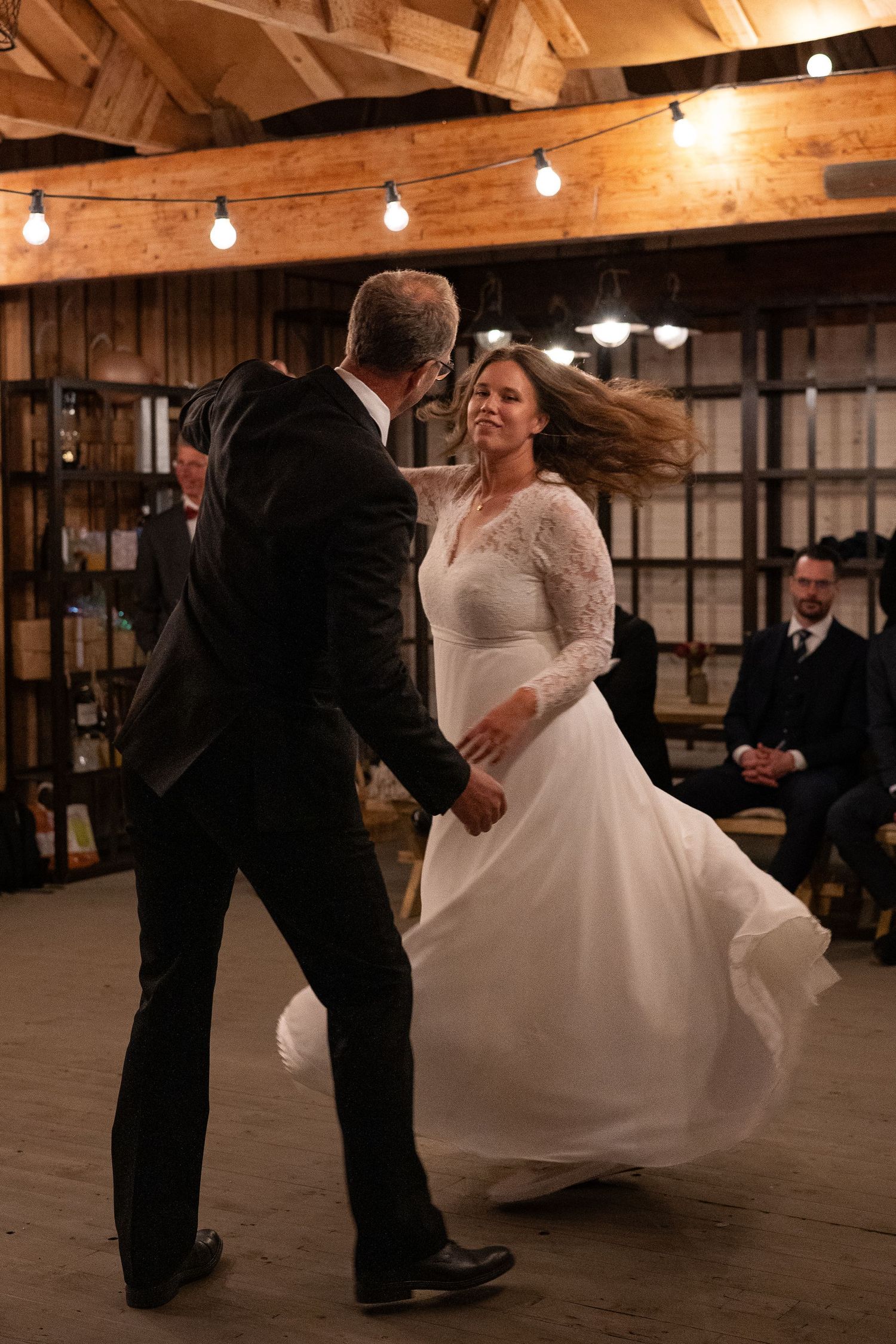 Bride and groom share their first dance in a rustic barn venue with warm string lights.