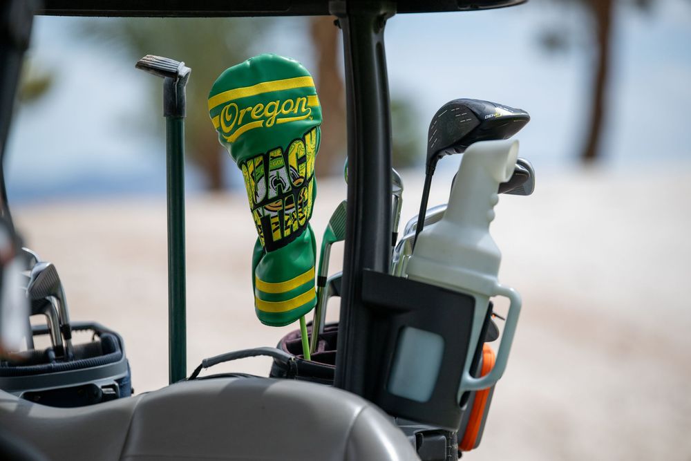 Oregon Ducks branded golf club head cover in green and yellow on a golf cart bag with clubs and accessories.