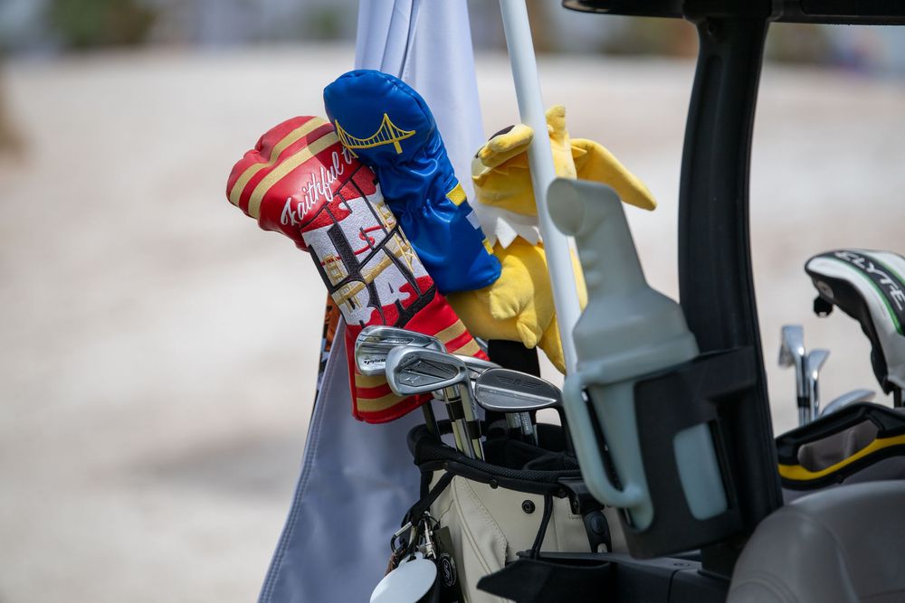 Colorful golf club head covers on a golf cart bag, featuring red, blue, and yellow novelty designs.
