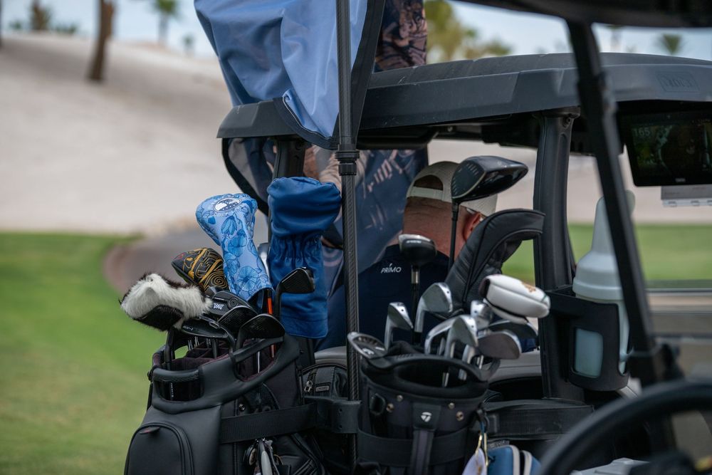 Golf bags filled with clubs and colorful headcovers loaded on the back of a golf cart on a sunny day.