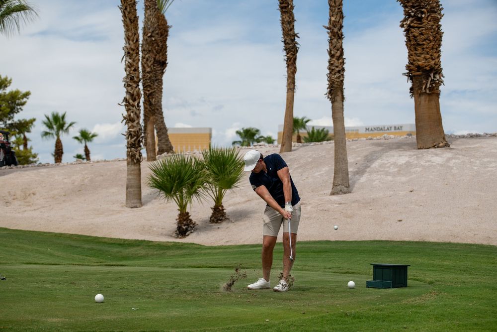 Golfer preparing to swing on a desert golf course surrounded by palm trees and sandy terrain.