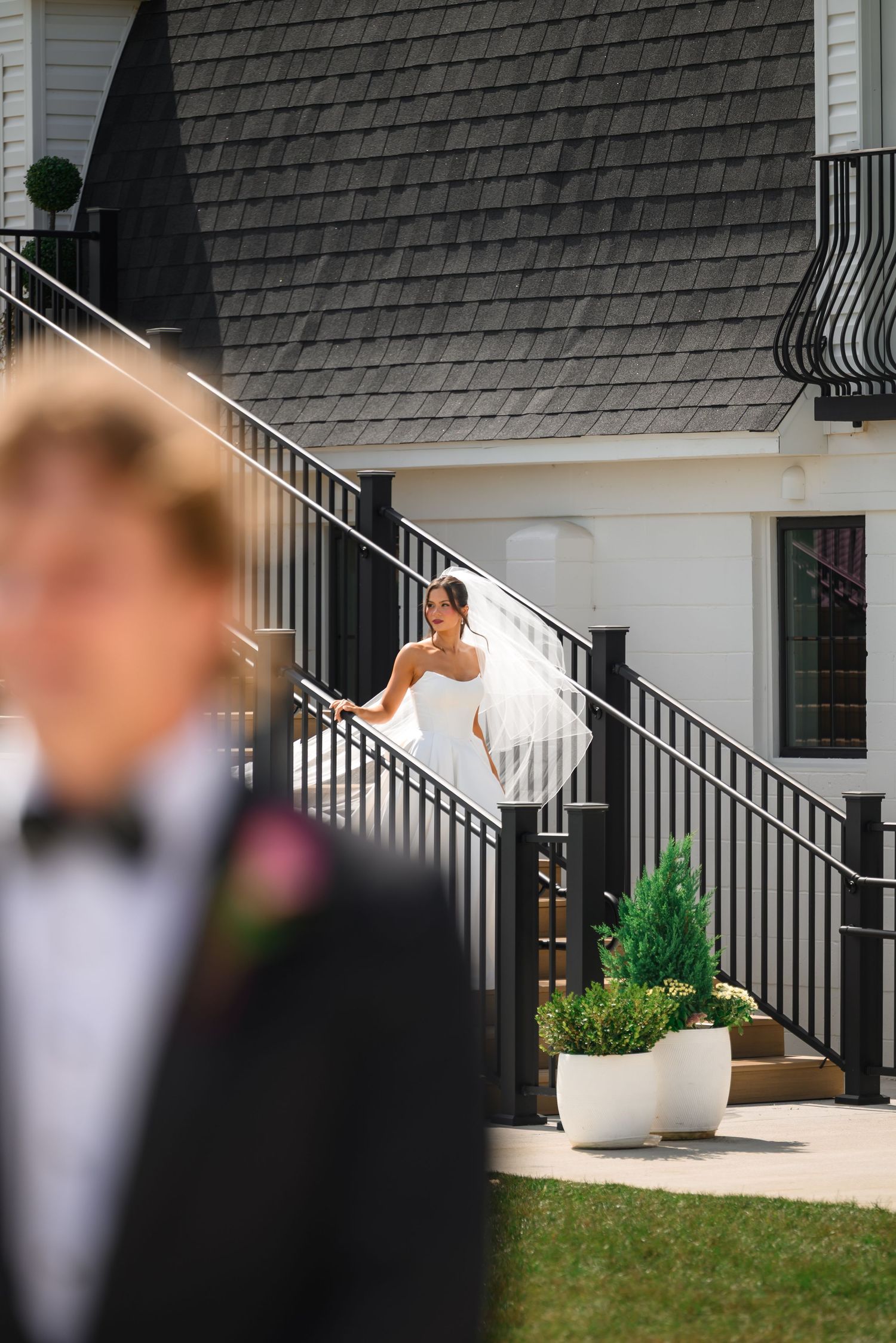 Bride in white gown descends black staircase toward groom in tuxedo during outdoor wedding first look.