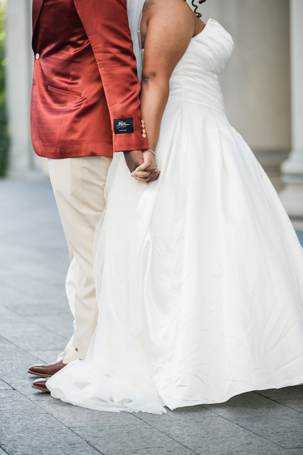 Bride in white gown and groom in red jacket holding hands at outdoor wedding ceremony.