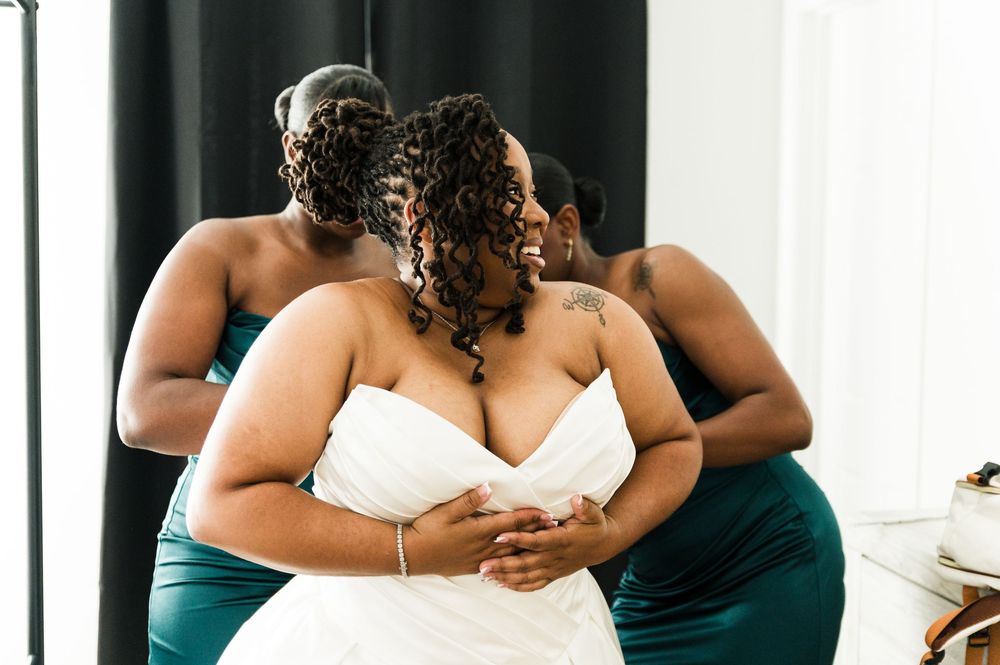 Bride in white strapless gown embraced by bridesmaids in teal dresses during wedding preparations.