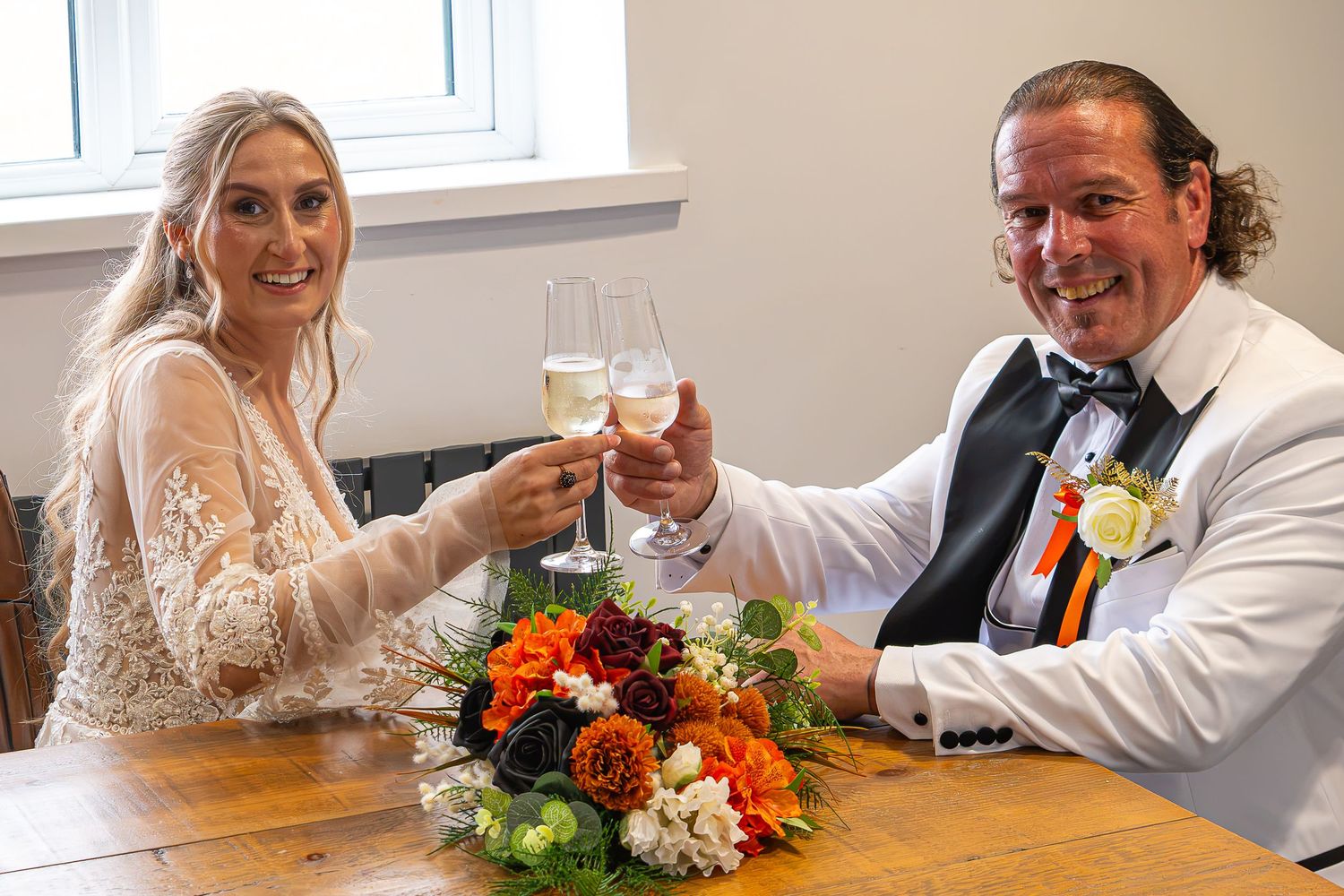 Bride and groom toasting with champagne glasses at wedding table with colorful floral centerpiece.Yorkshire, Sheffield, Lincolnshire, UK