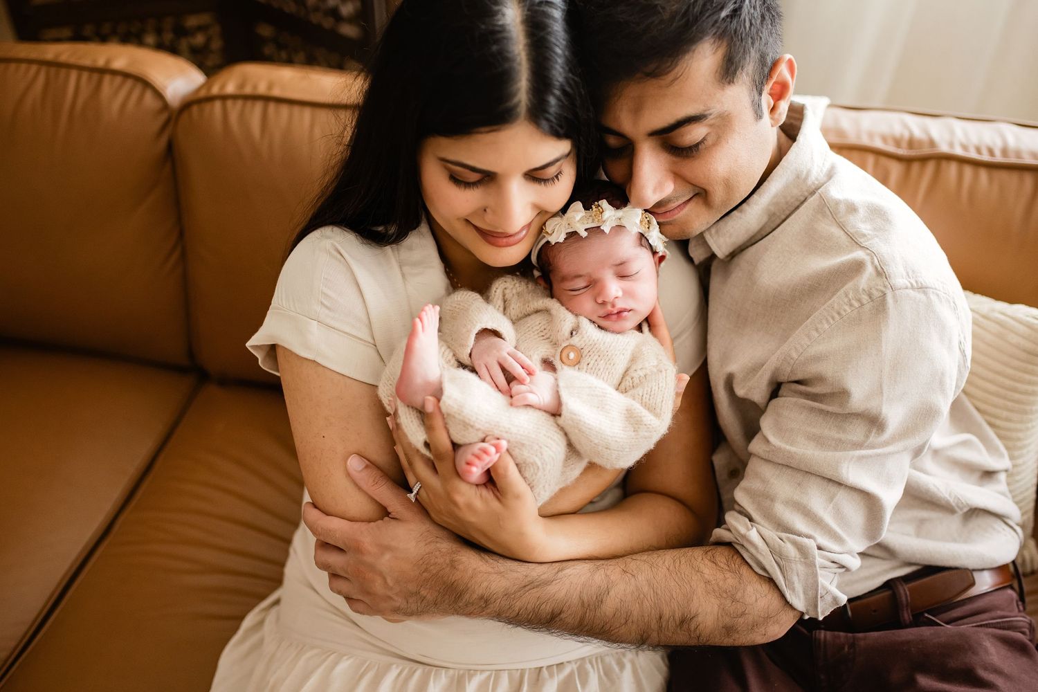 Parents lovingly cradle their swaddled newborn baby on a couch during an intimate in-home newborn photography session.