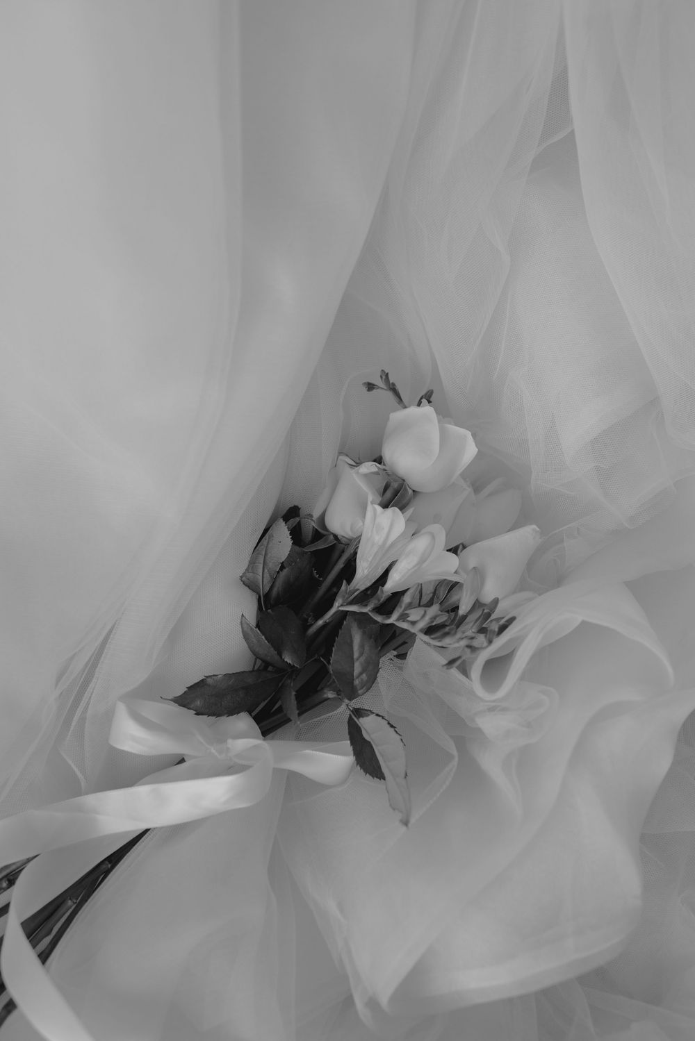 Delicate bridal bouquet of white roses nestled in flowing tulle fabric, captured in black and white.