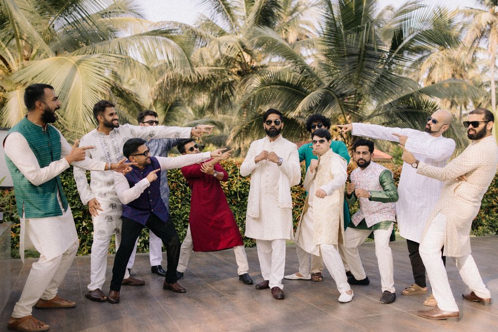 Group of men in traditional Indian attire dancing joyfully outdoors at a wedding celebration with tropical palms backdrop.