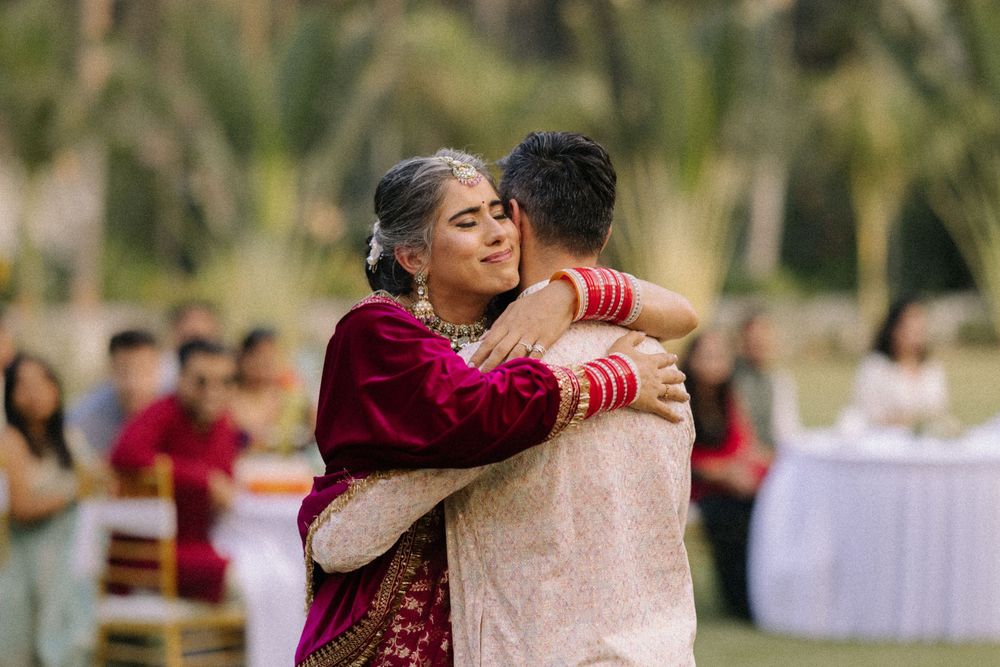 Emotional mother and son embrace during an outdoor Indian wedding ceremony, wearing traditional attire with guests in background.