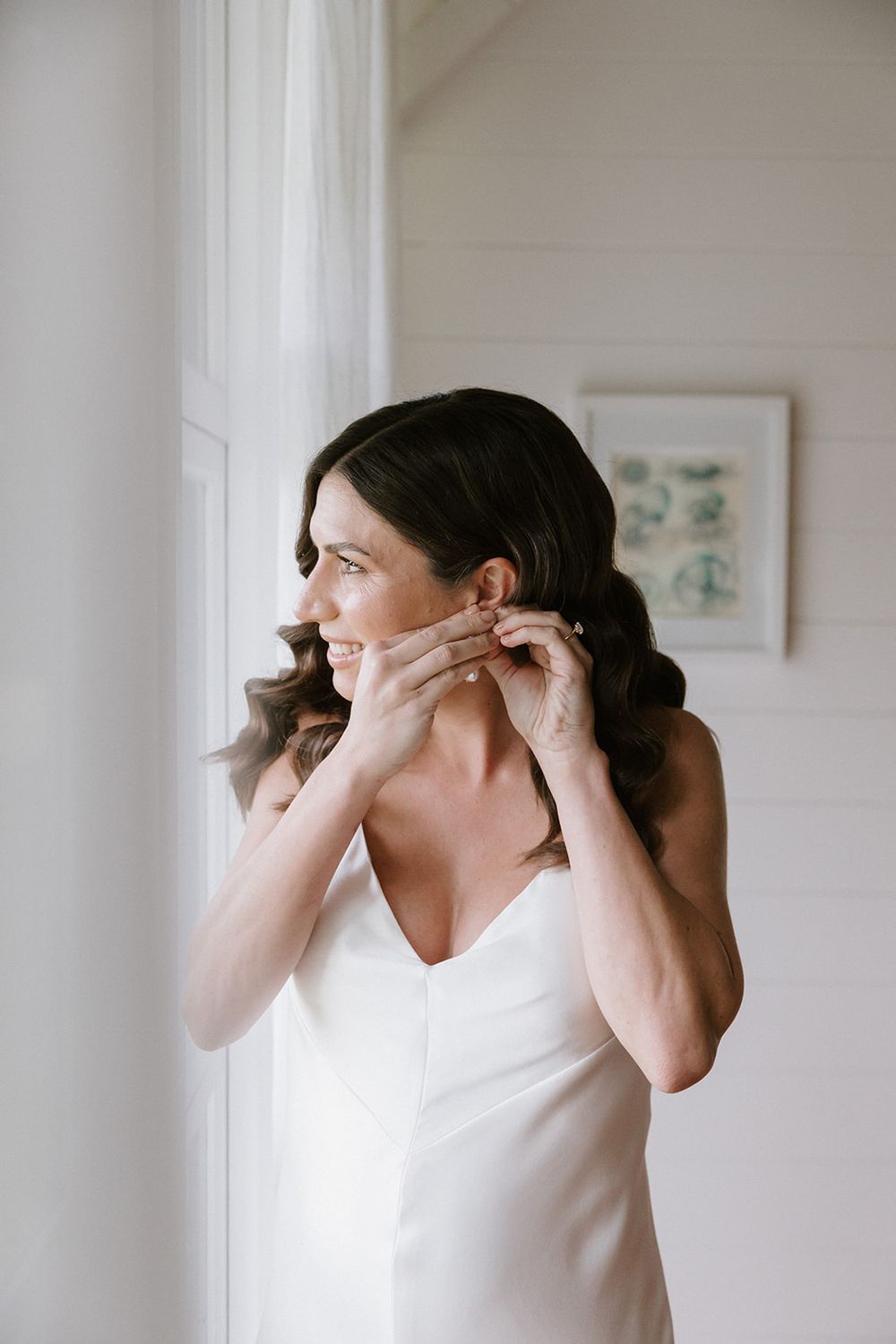 Someone adjusting jewelry or accessories while getting ready in a light-filled room with white walls.