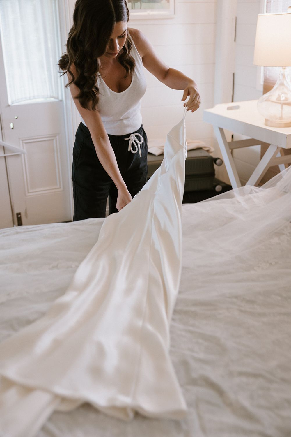 A white wedding dress being fluffed and arranged on a bed in preparation.