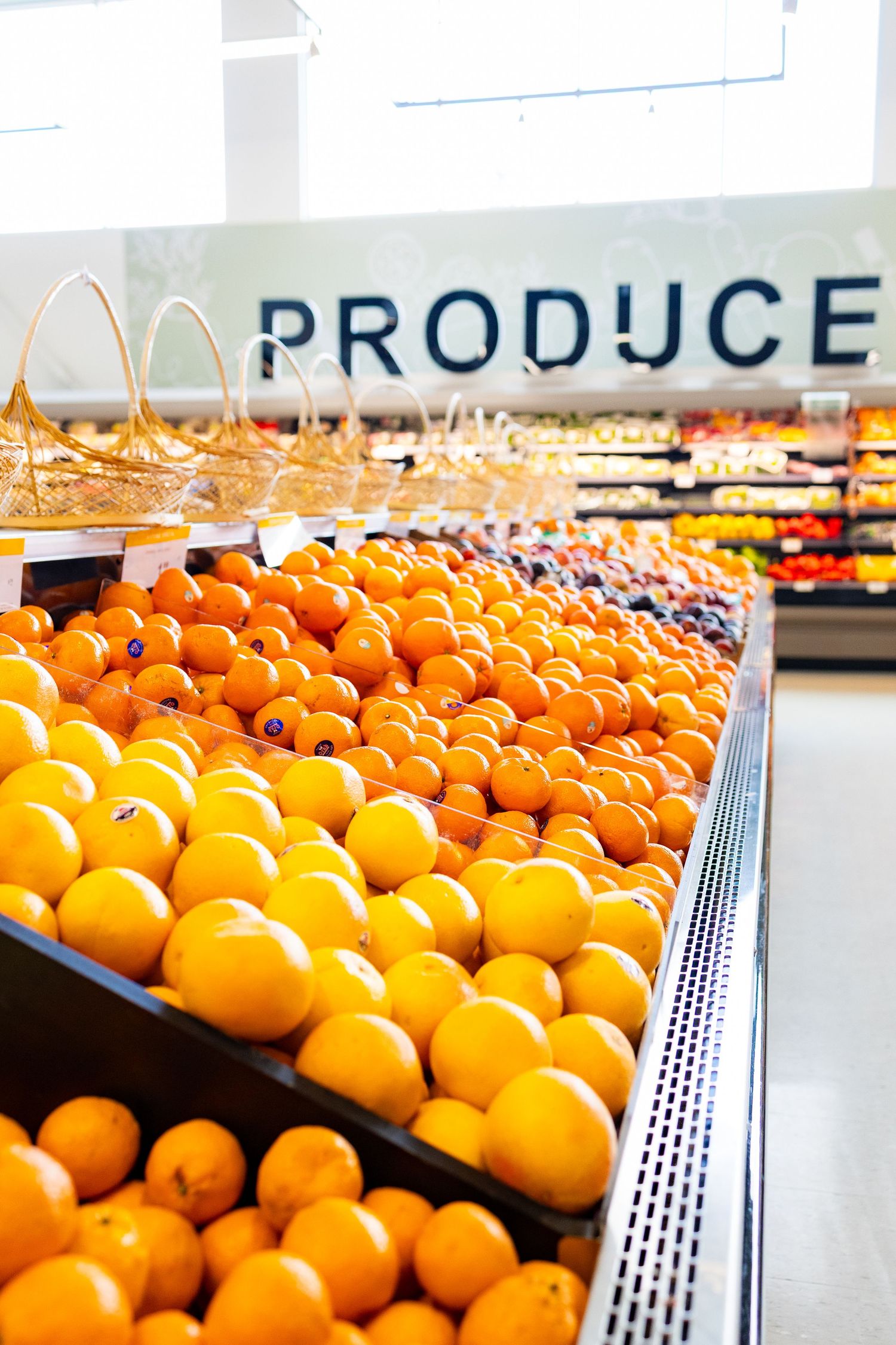 Fresh oranges displayed in abundance on a supermarket produce section shelf under bright store lighting.