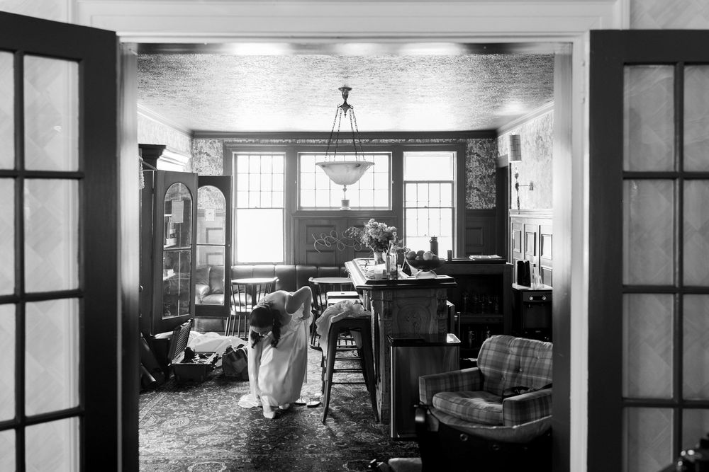 Black and white photo of a bride standing in an elegantly furnished room with French doors and vintage decor.
