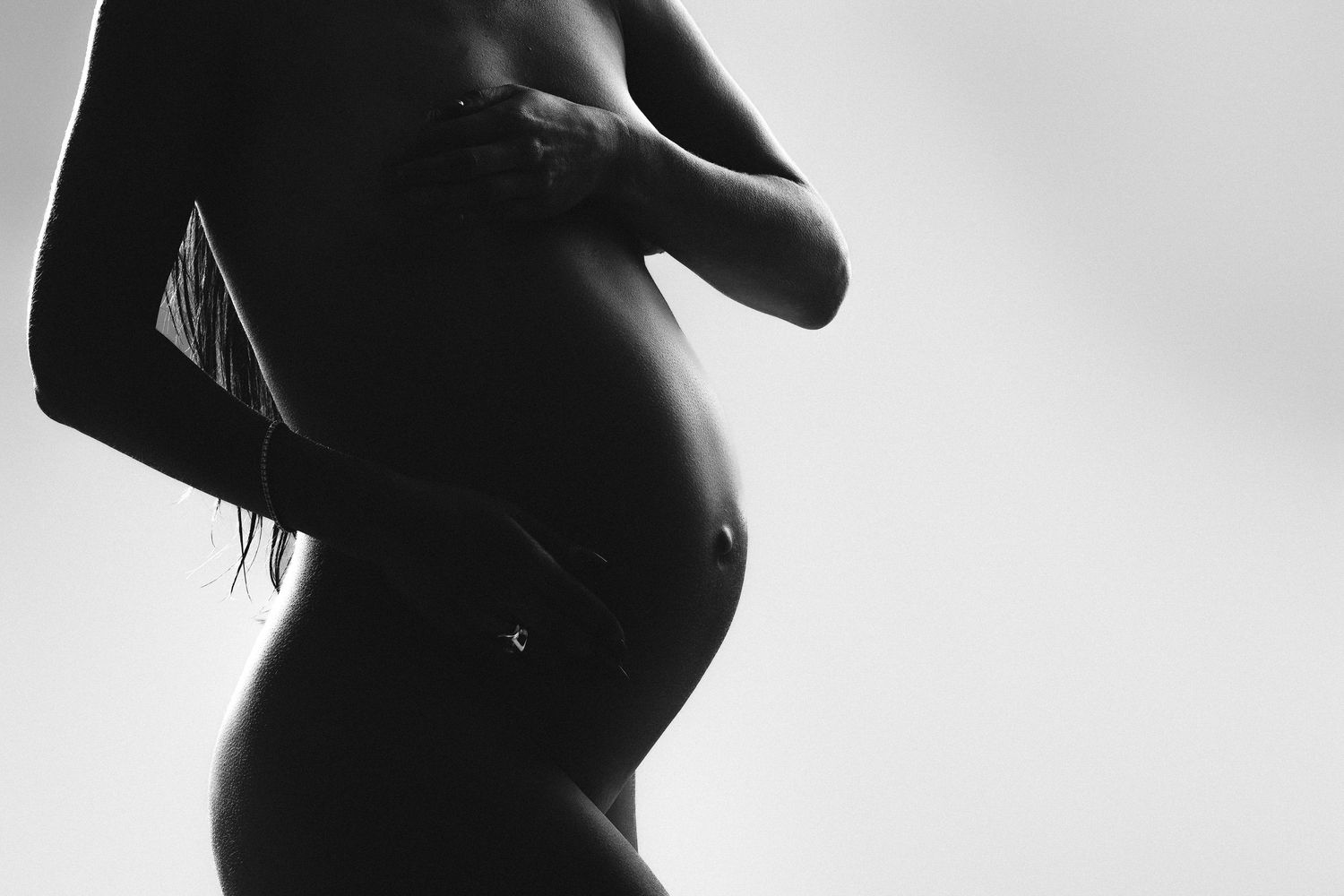Black and white silhouette of a pregnant woman cradling her baby bump, maternity photography art.