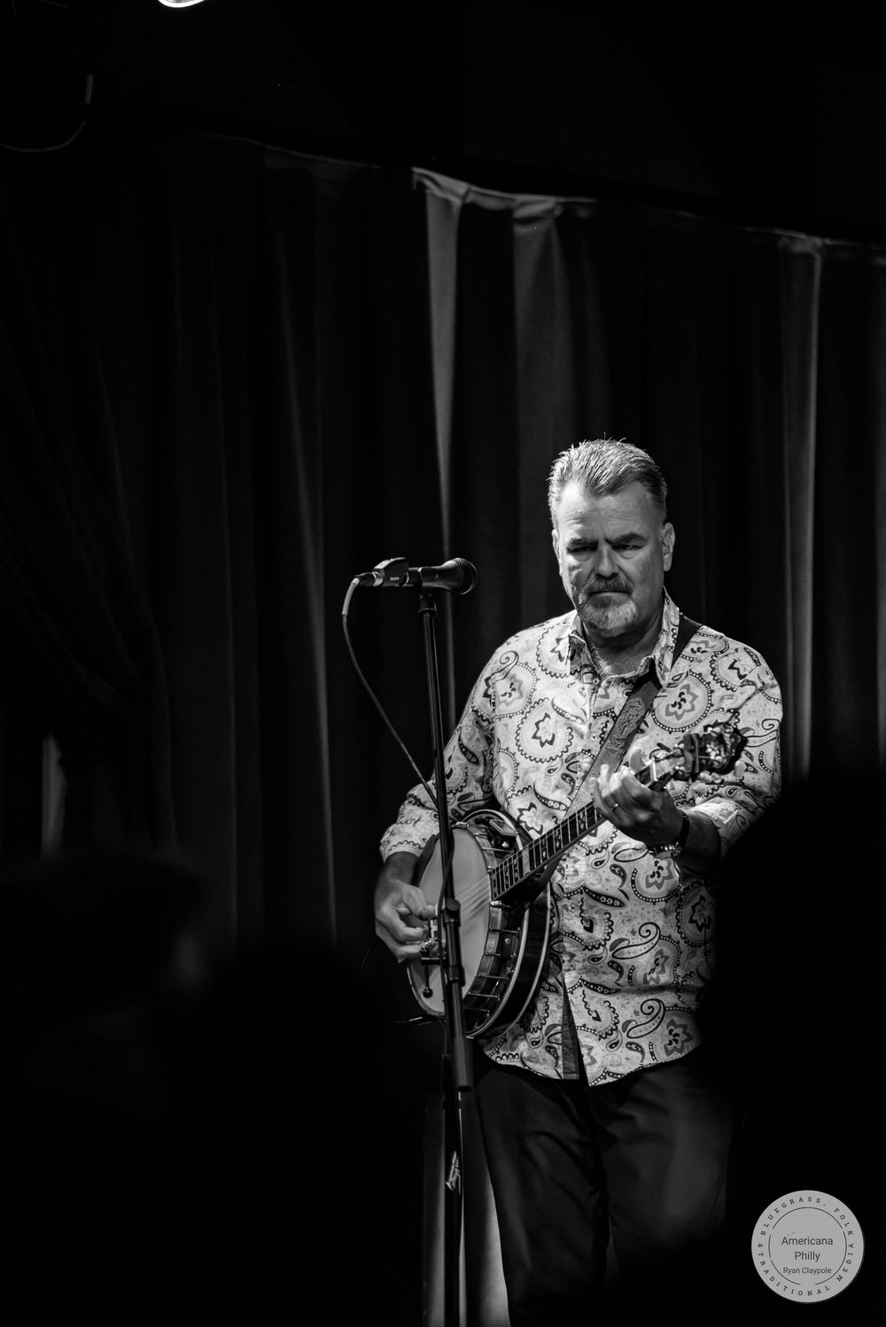 Black and white photo of a man playing banjo on stage at a live music performance.