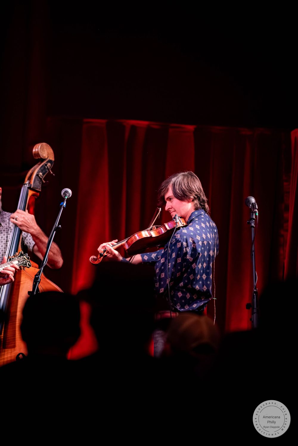 Musician playing violin on stage with a double bass player beside them, performing under red stage lighting.