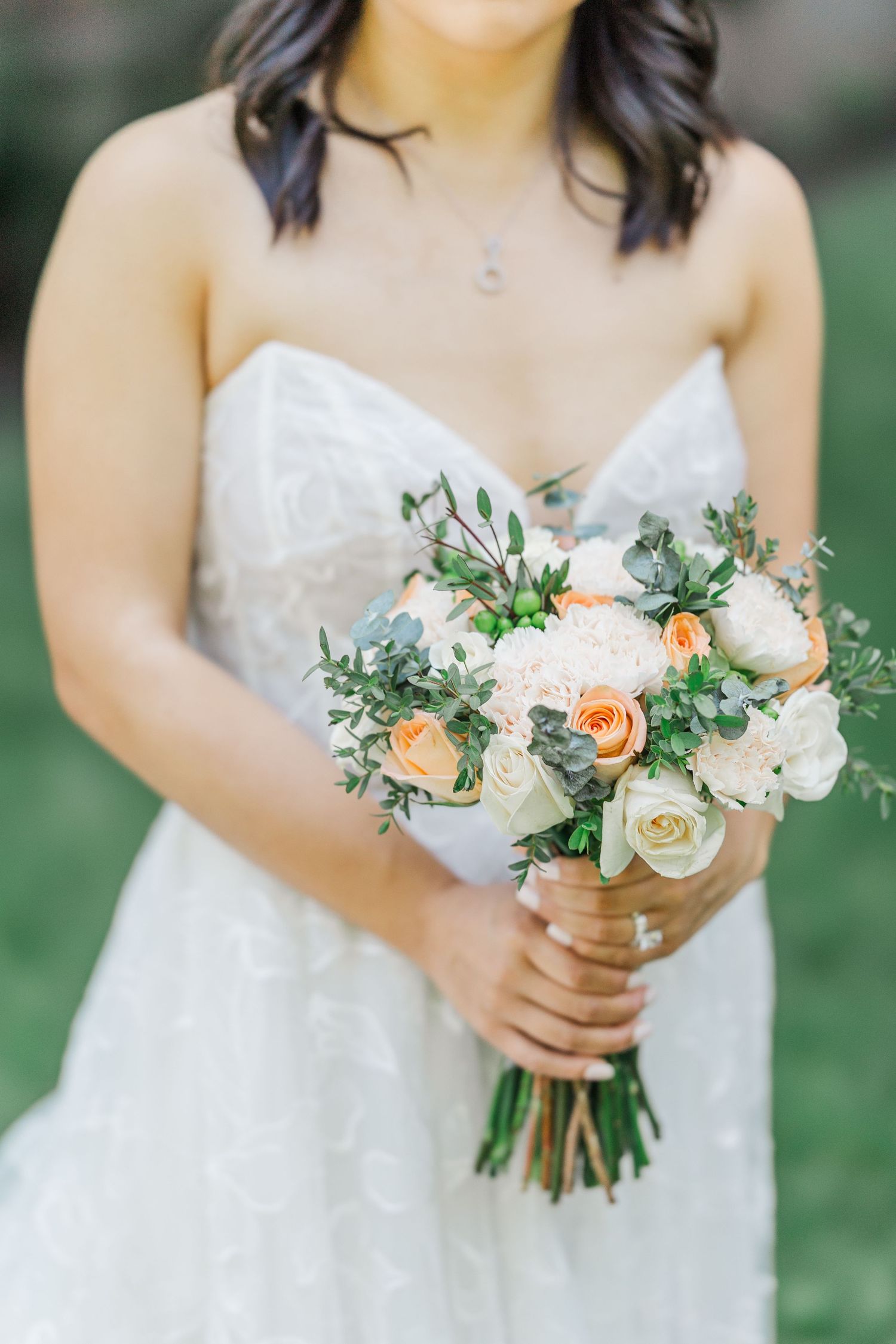 Bride in strapless lace gown holding a bouquet of peach and white roses with eucalyptus greenery.