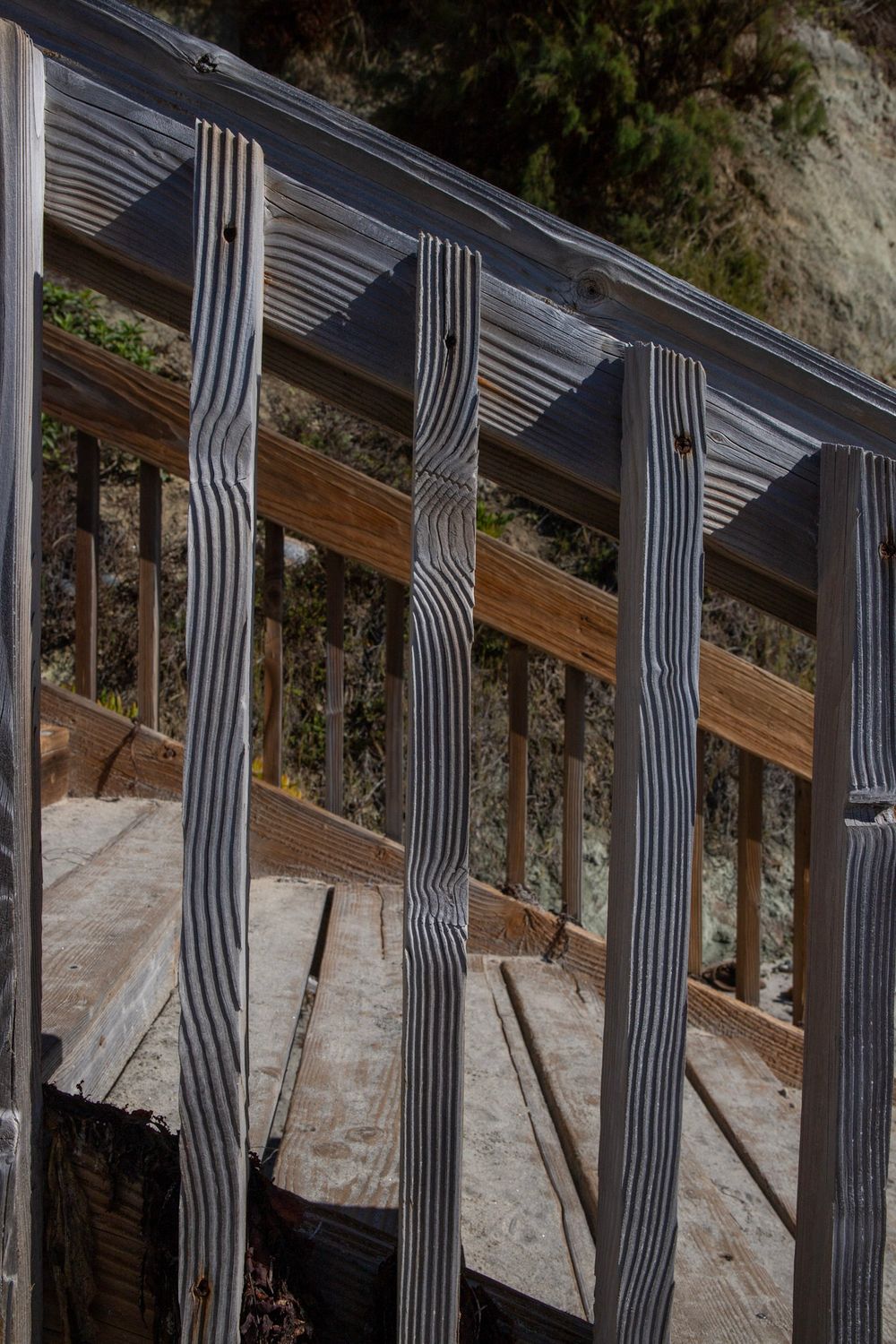Weathered wooden deck railing with vertical spindles casting striped shadows on aged planks outdoors.