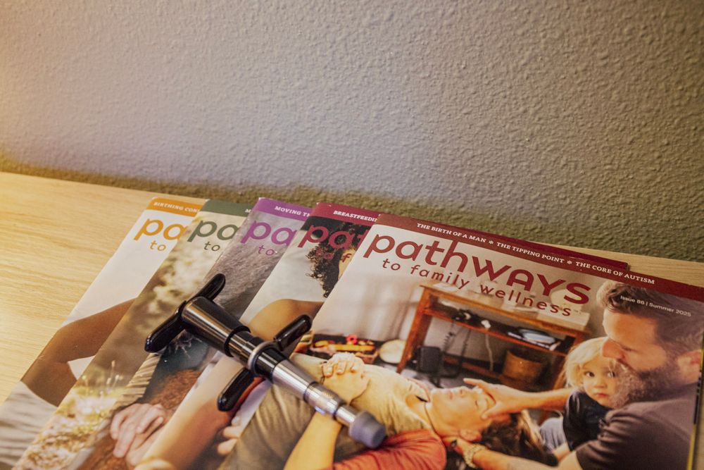 Stack of Pathways to Family Wellness magazines on a wooden surface with a pen resting on top.