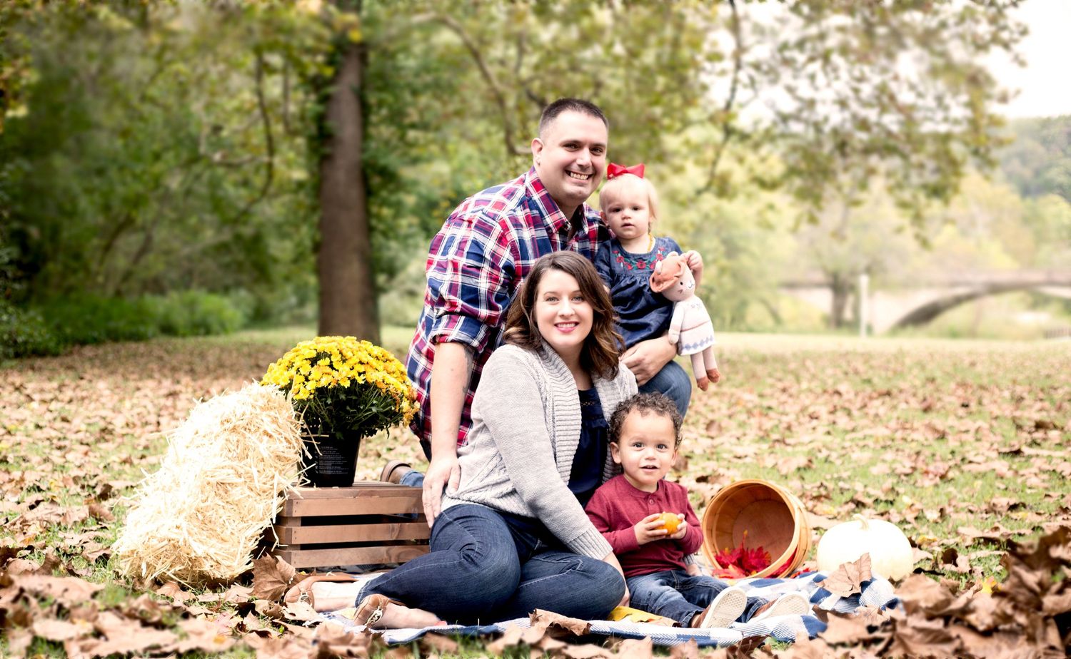 Happy family of four enjoying an autumn outdoor portrait session surrounded by colorful fallen leaves.