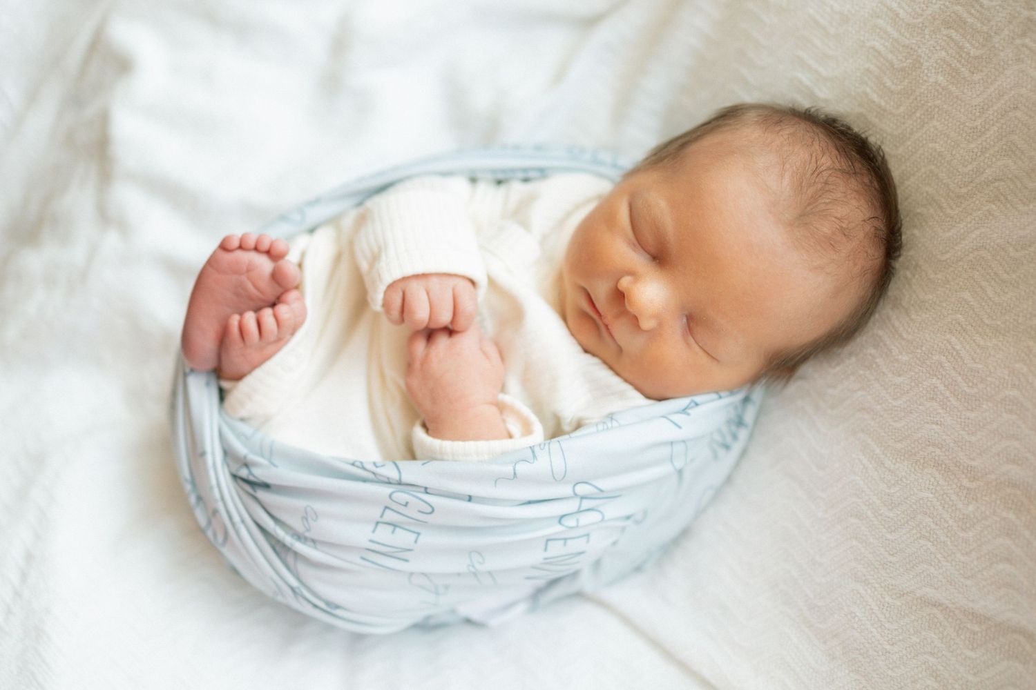 Peaceful newborn baby sleeping curled up in a light blue basket on a soft white blanket at University of Tennessee Medical Center.