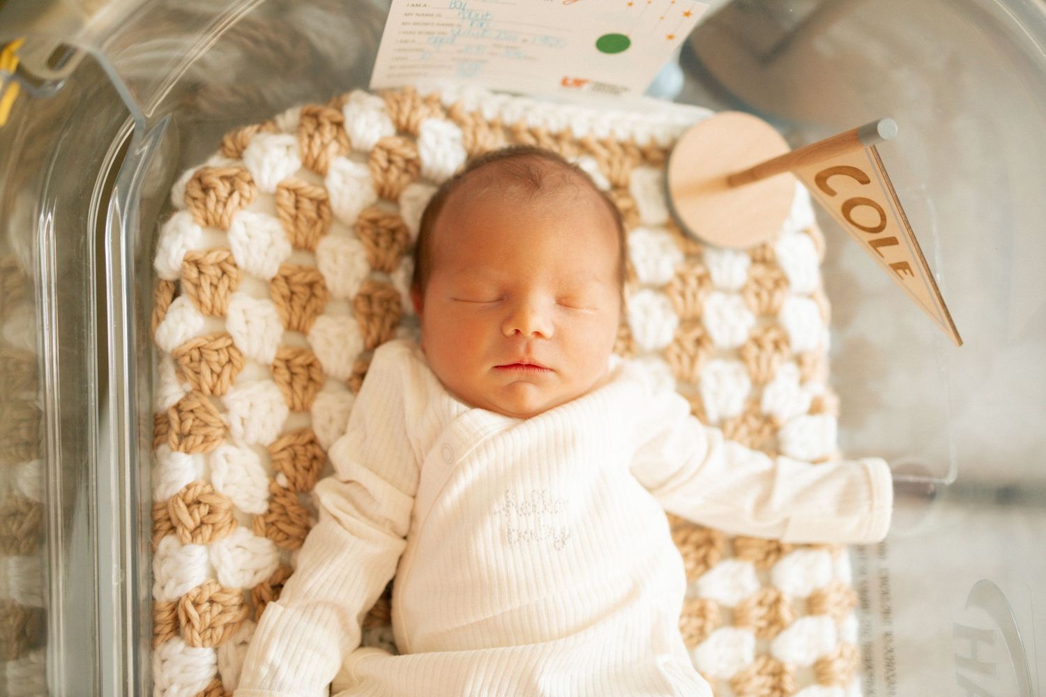 Newborn baby sleeping peacefully in hospital bassinet on crochet blanket with name sign at University of Tennessee Medical Center.