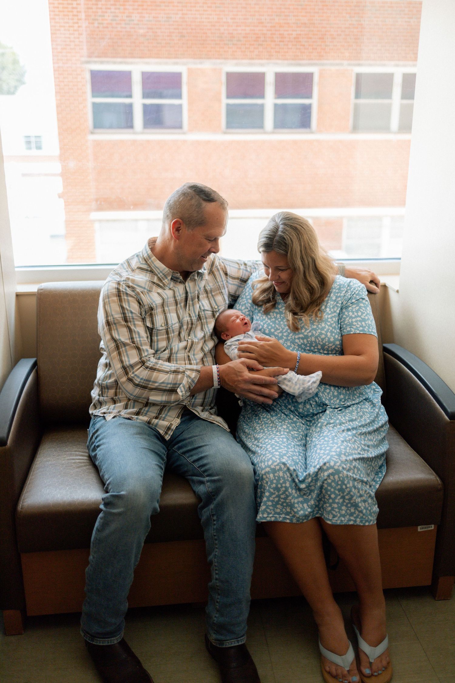 New parents sitting on hospital couch admiring their newborn baby, with brick building visible through window at University of Tennessee