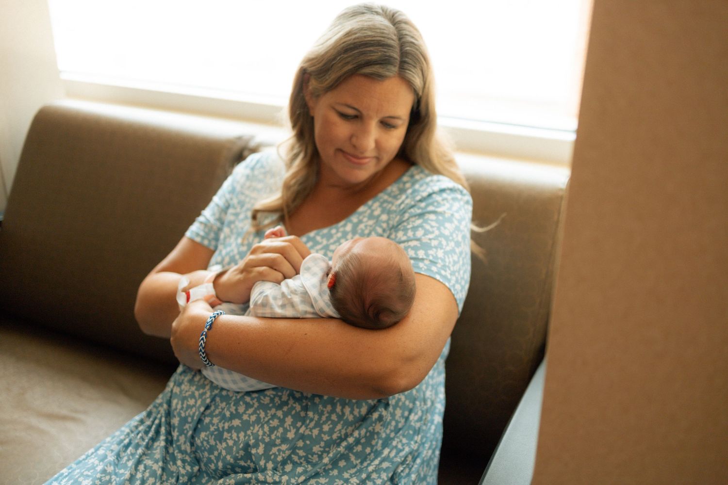 Mother in floral dress tenderly holding newborn baby while sitting on sofa at University of Tennessee Medical Center.