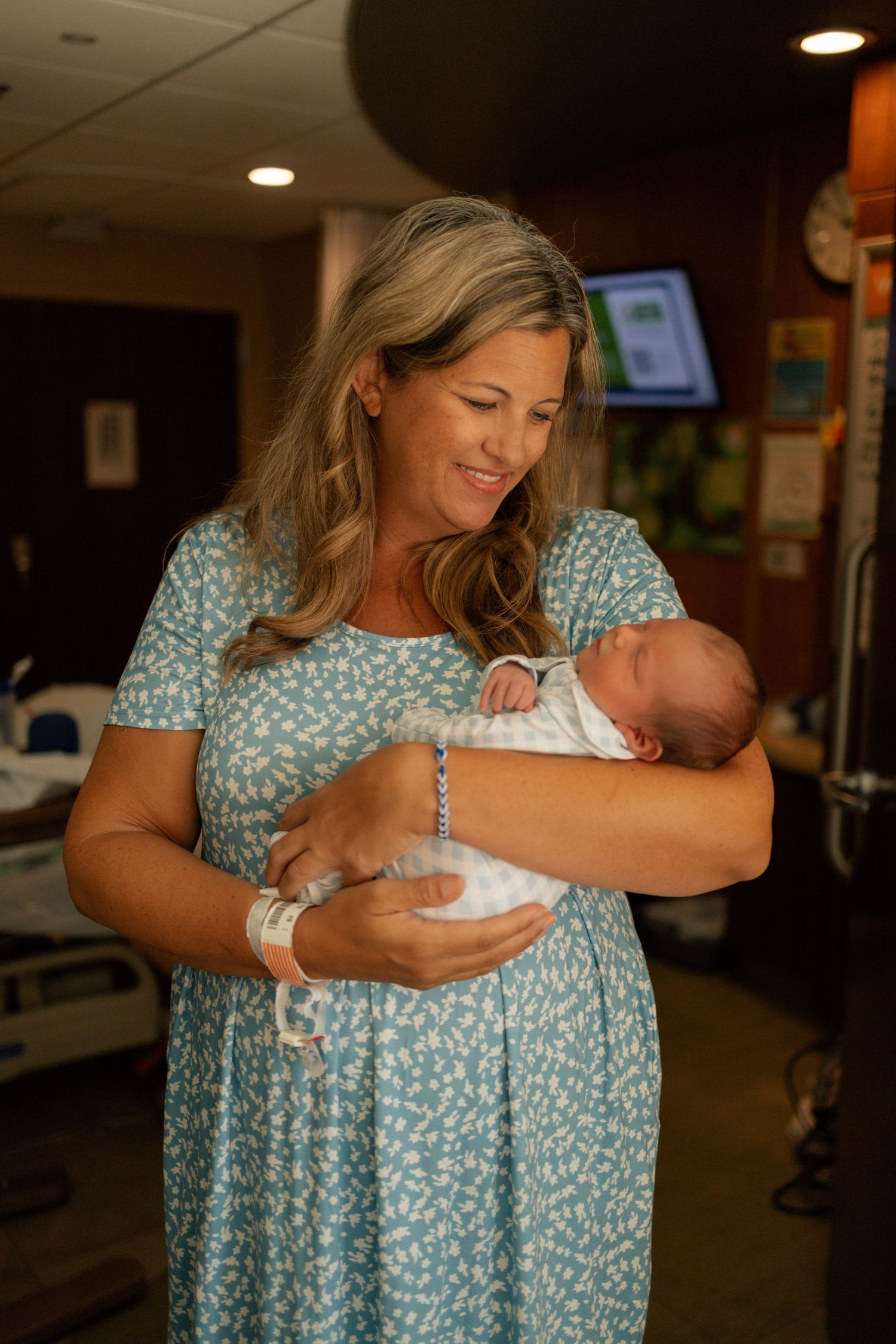 A smiling mother in a floral dress holds her newborn baby in a hospital room after giving birth at University of Tennessee Medical Center.