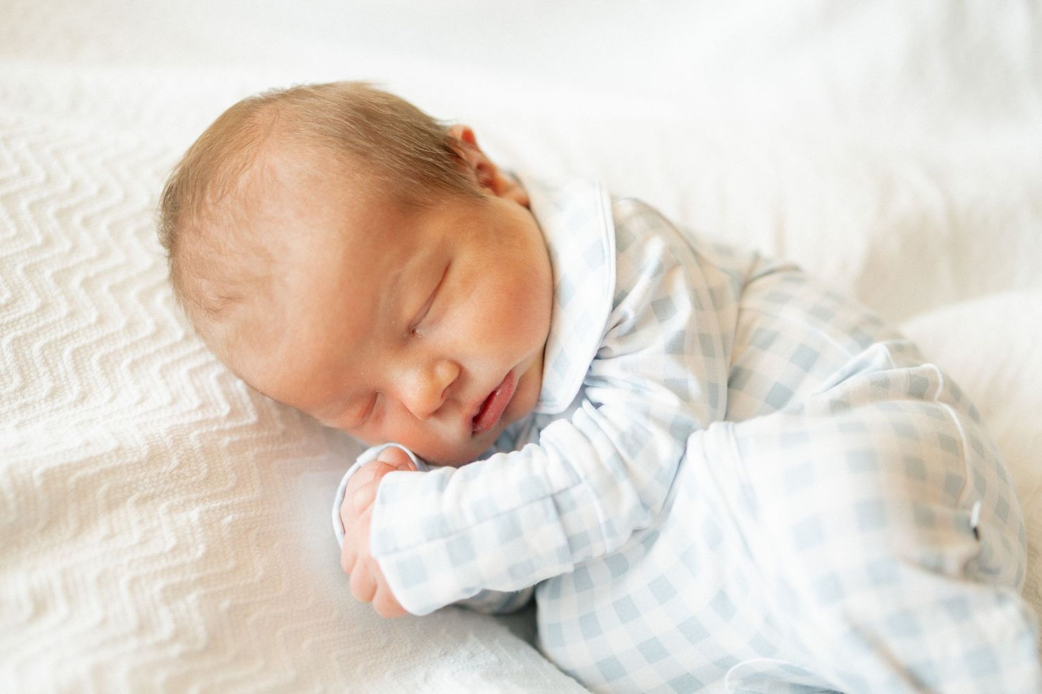 Peaceful newborn baby sleeping on white blanket with tiny hands tucked under chin at University of Tennessee.
