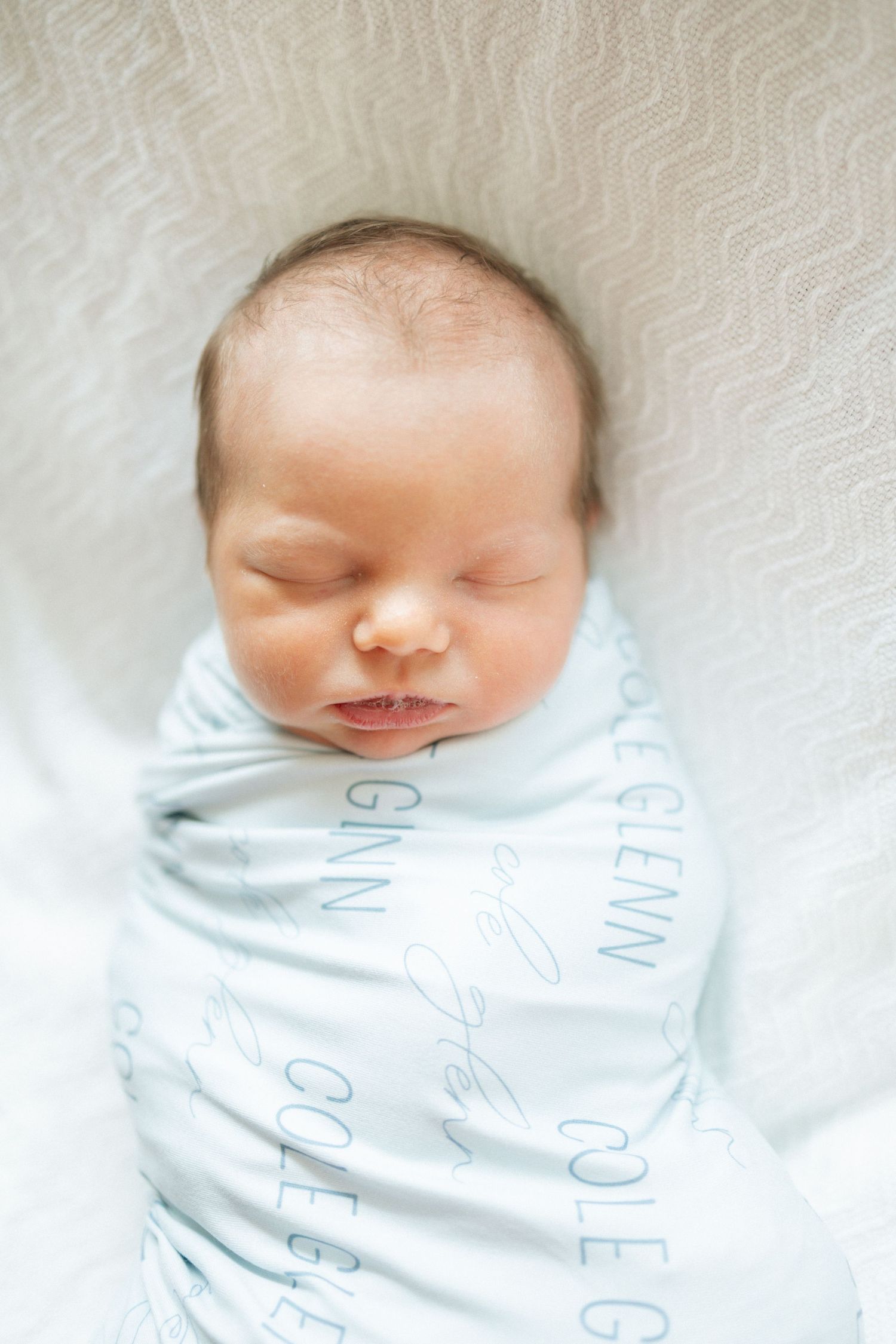 Sleeping newborn baby swaddled in a personalized light blue blanket with the name Cole Glenn at University of Tennessee Medical Center.