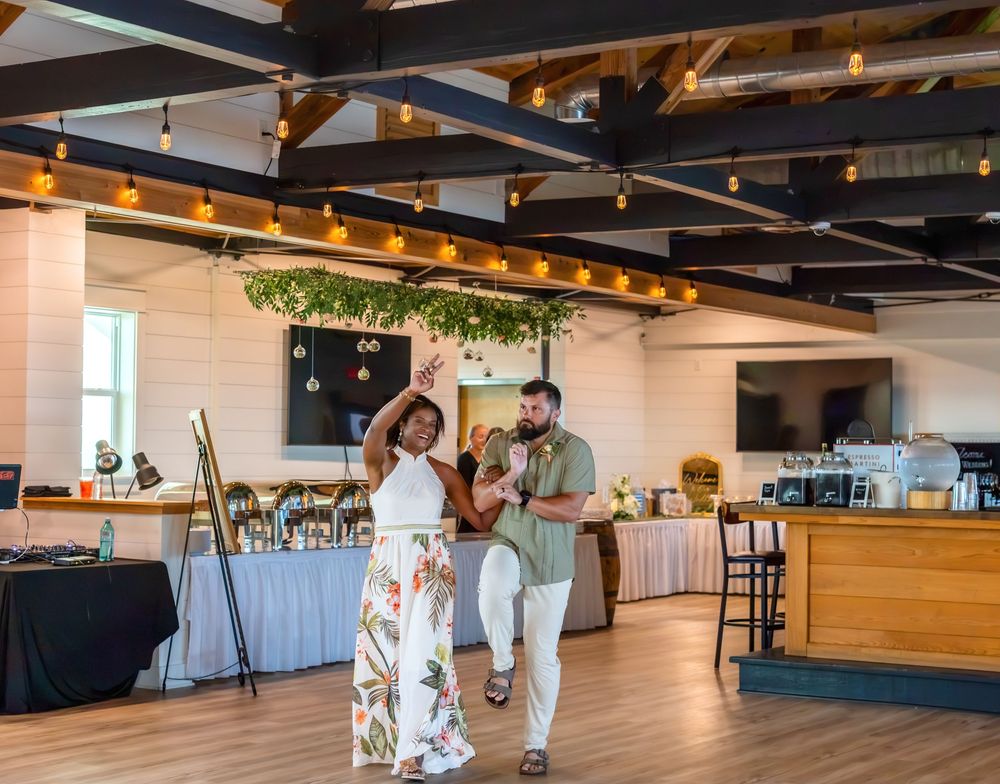Couple dancing together in elegant event venue with string lights and greenery decor.