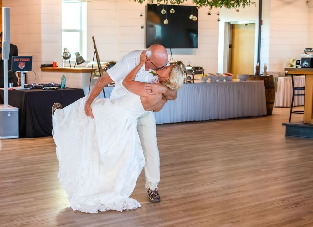 Groom dips bride in elegant first dance at wedding reception on hardwood floor.
