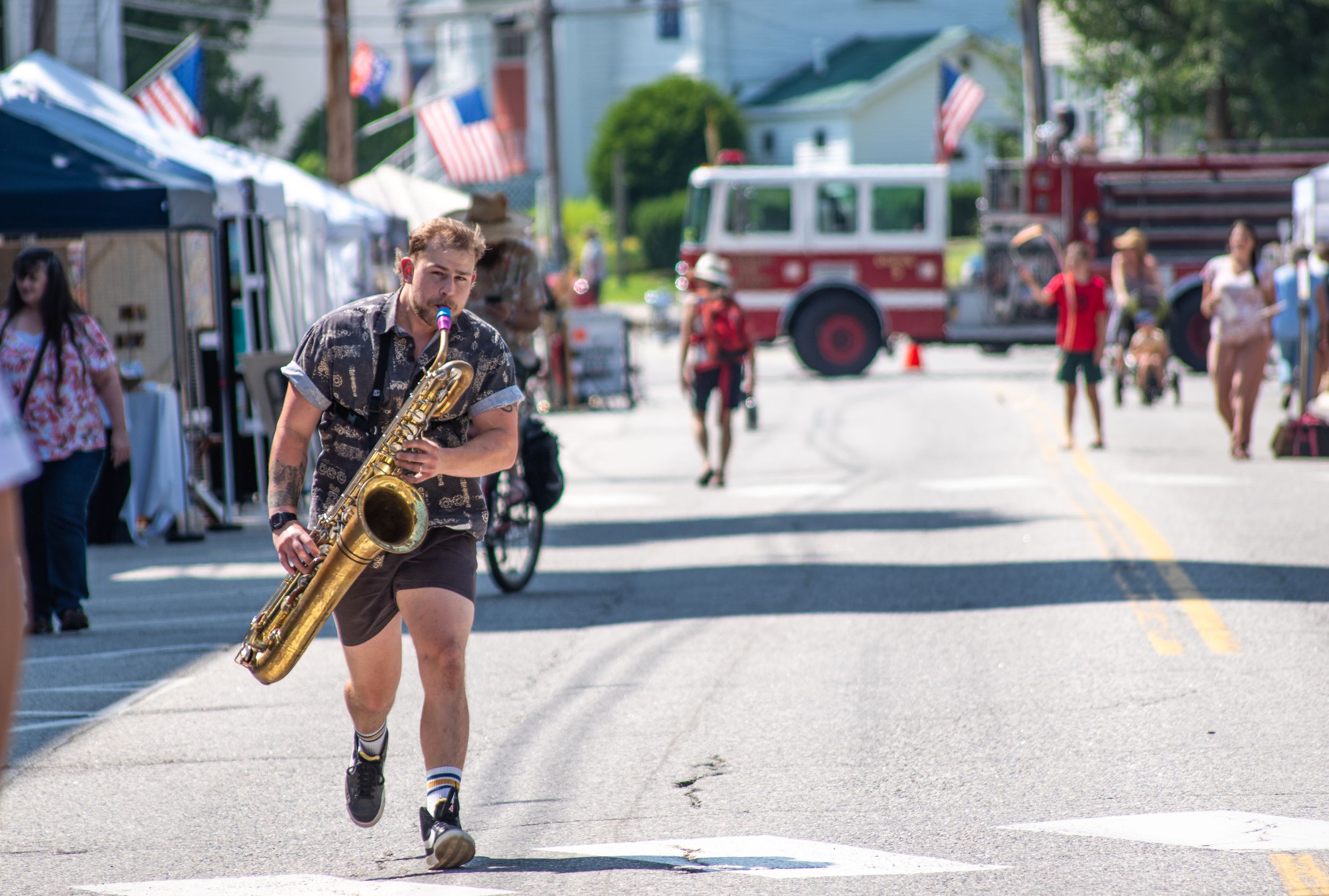 Musician playing saxophone while running down a street during an outdoor summer festival parade.