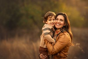 A smiling mother hugs her young son in a sunlit autumn field, both radiating joy and warmth.
