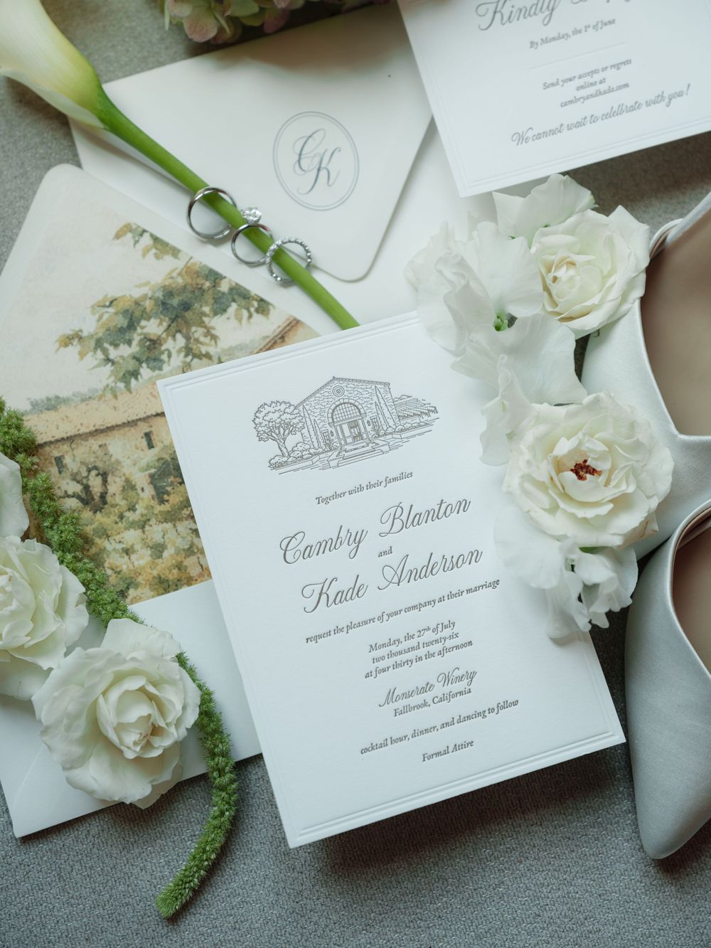 Elegant wedding invitation suite for Cambry Blanton and Kade Anderson with white roses, rings, and bridal shoes.