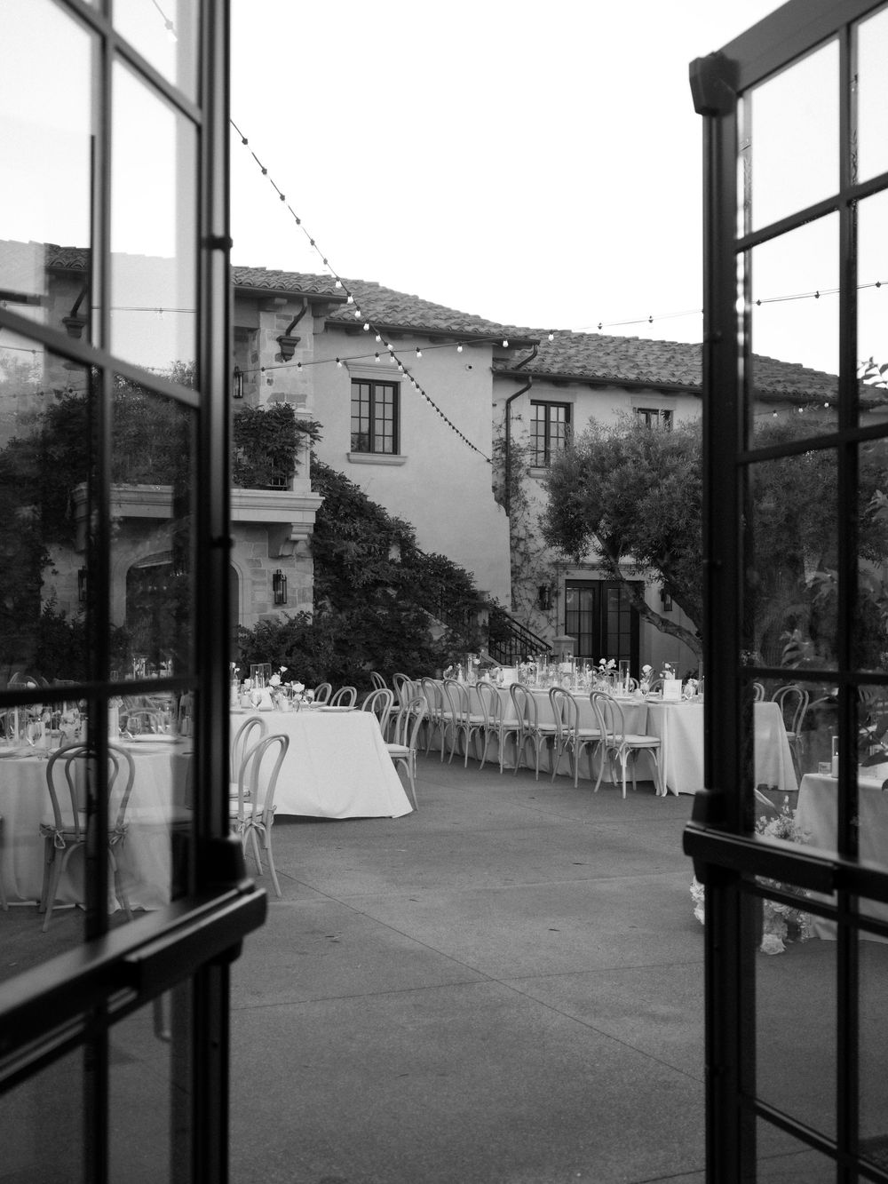 Black and white photo of an elegant outdoor wedding reception with long tables and string lights at a villa.