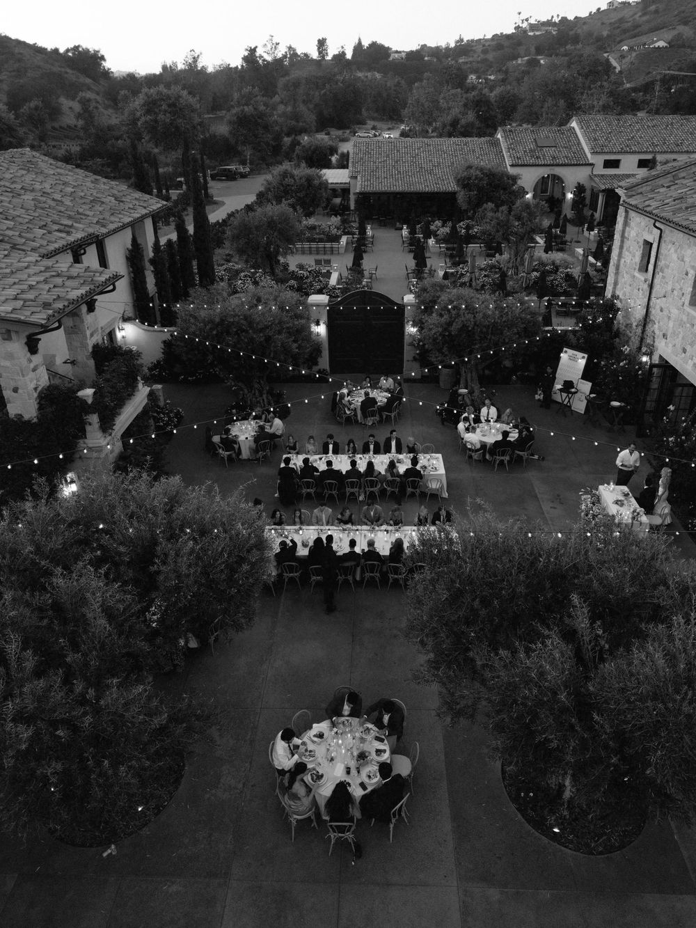 Aerial black and white view of an elegant outdoor wedding reception with string lights in a courtyard.