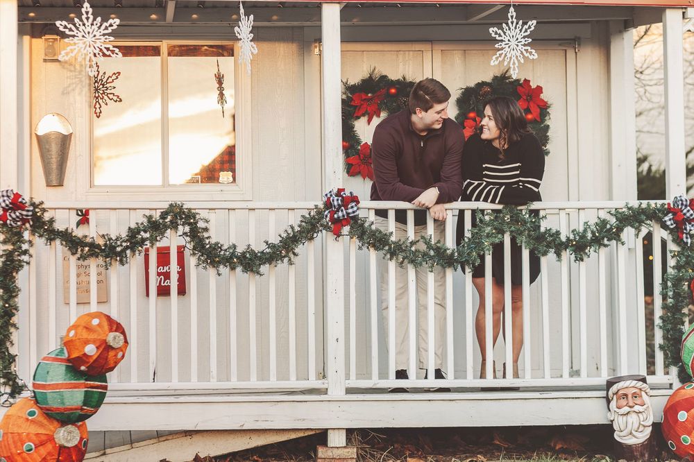 Couple sharing a romantic moment on a Christmas-decorated porch with garland, wreaths, and holiday inflatables.