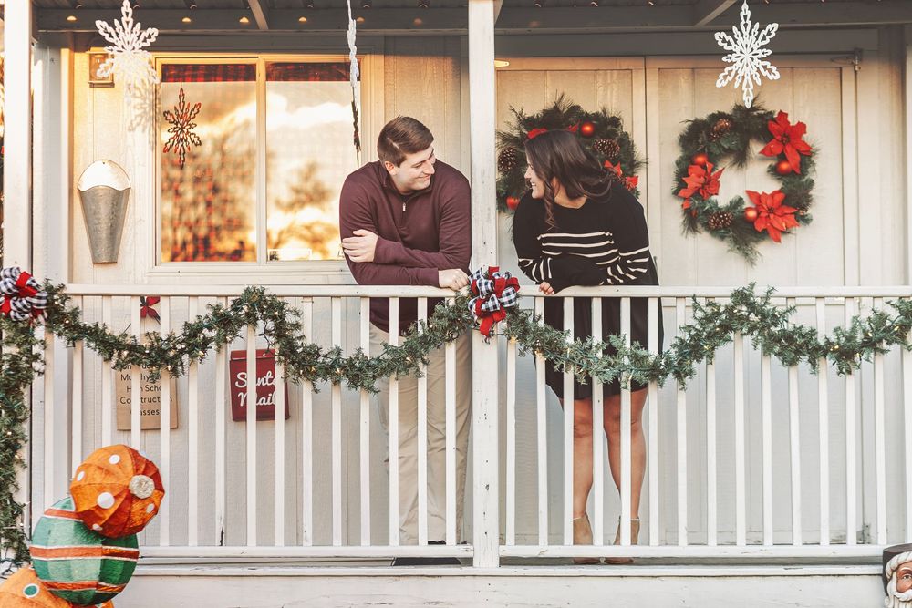Couple sharing a romantic moment on a Christmas-decorated porch with garland, wreaths, and holiday ornaments.