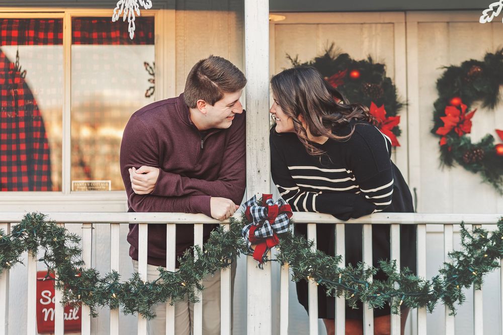 Couple sharing a romantic moment on a festive Christmas-decorated porch with garland and wreaths.