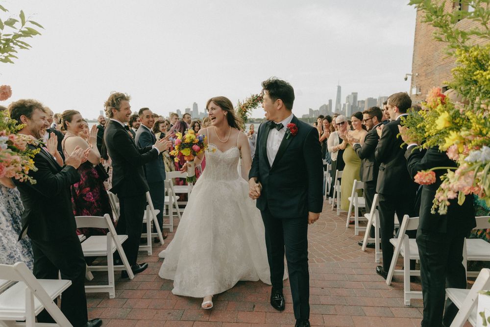 Bride and groom walking down the aisle at an outdoor rooftop wedding with floral decor.