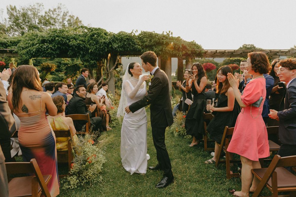 Newlyweds kissing while walking down the aisle at a lush outdoor garden wedding ceremony.