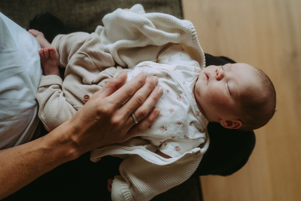 Parent cradling a sleeping newborn baby dressed in a white onesie, held gently in loving arms.