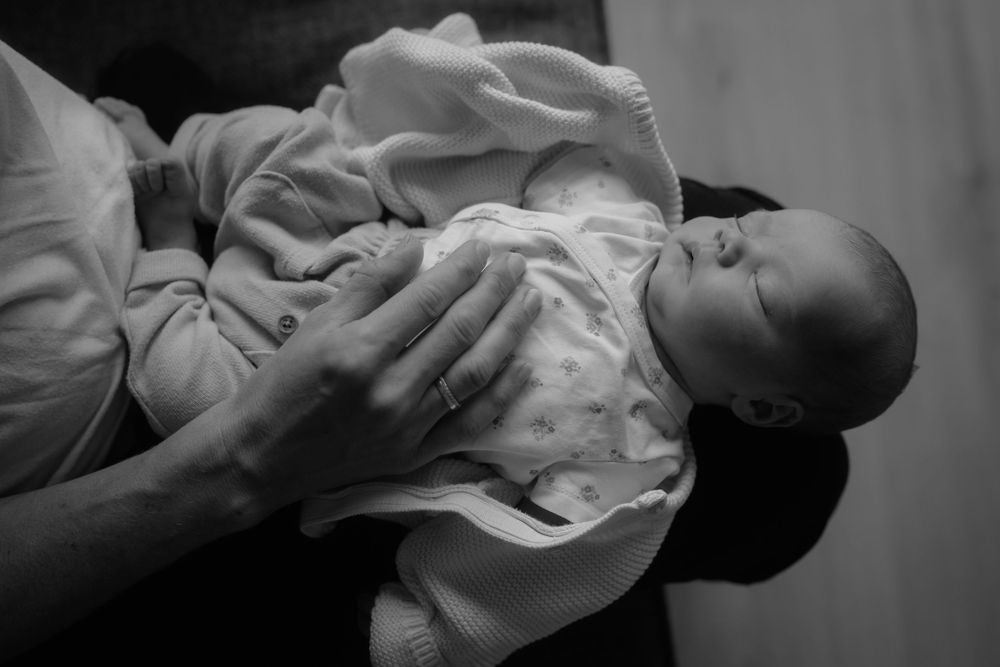 Black and white photo of a newborn baby being cradled gently in an adult's hands.