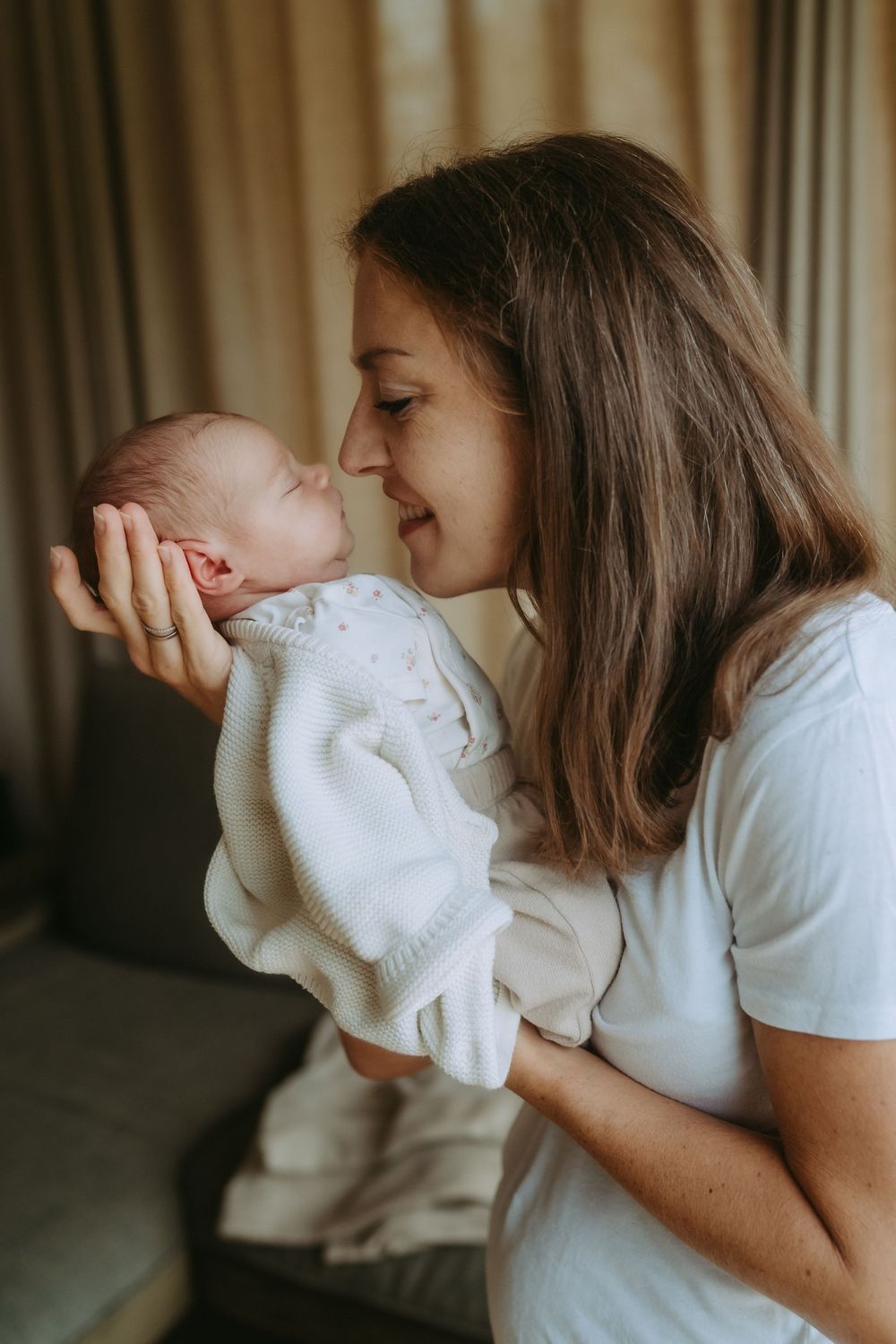 A mother tenderly holds her newborn baby close, touching noses in a loving moment at home.