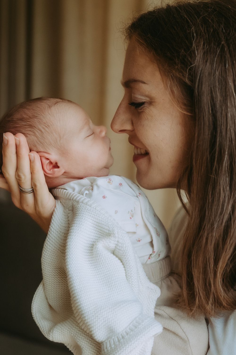 A smiling mother tenderly holds her newborn baby close, touching noses in a warm and loving embrace.