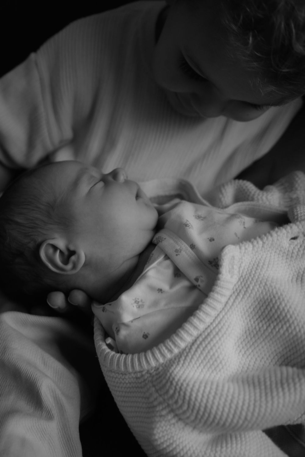 Close-up black and white photo of a parent tenderly cradling a sleeping newborn baby.